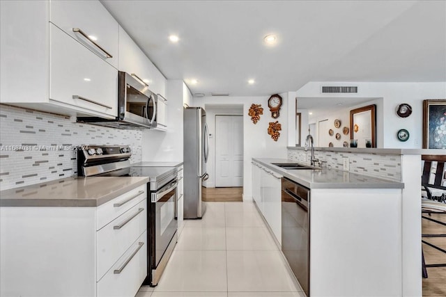 kitchen with sink, light tile patterned flooring, a kitchen bar, white cabinetry, and appliances with stainless steel finishes