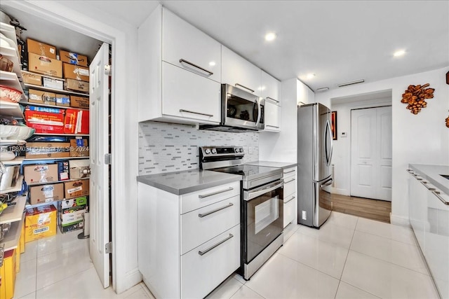 kitchen featuring appliances with stainless steel finishes, decorative backsplash, white cabinetry, and light tile patterned flooring