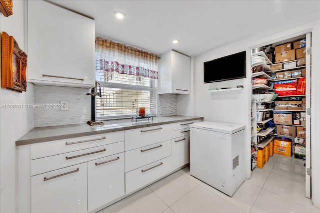 kitchen featuring decorative backsplash, white cabinetry, light tile patterned flooring, and refrigerator