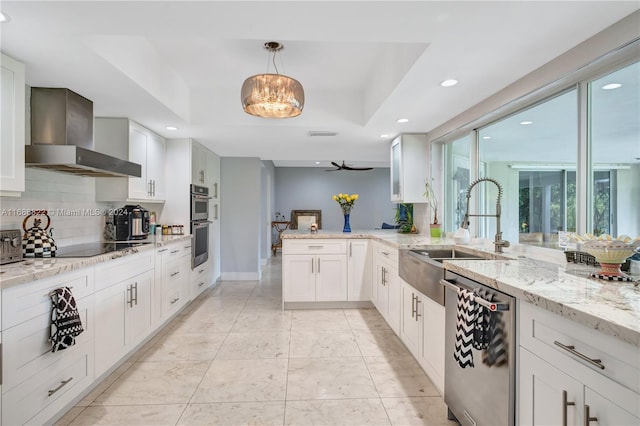 kitchen featuring white cabinets, wall chimney exhaust hood, stainless steel dishwasher, and decorative light fixtures