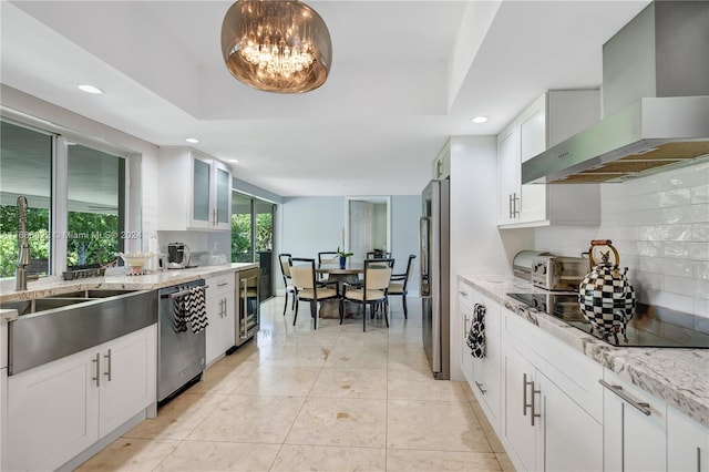 kitchen featuring white cabinets, appliances with stainless steel finishes, light stone counters, and wall chimney range hood