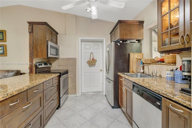 kitchen with stainless steel appliances, dark stone counters, vaulted ceiling, light tile patterned floors, and sink