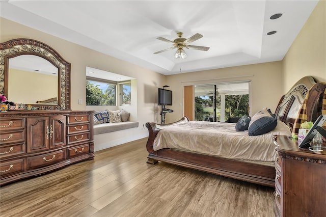 bedroom with ceiling fan, multiple windows, a raised ceiling, and light wood-type flooring