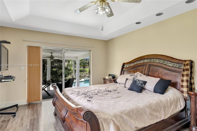 bedroom with ceiling fan, wood-type flooring, a tray ceiling, and access to outside