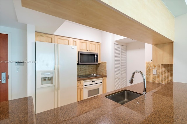 kitchen featuring light brown cabinetry, backsplash, white appliances, sink, and dark stone countertops