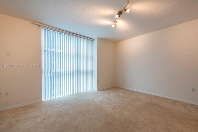 carpeted empty room with rail lighting and a textured ceiling