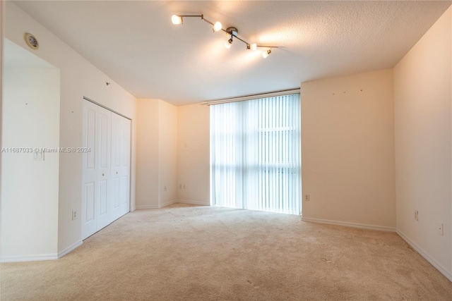 empty room with a textured ceiling, light colored carpet, and rail lighting