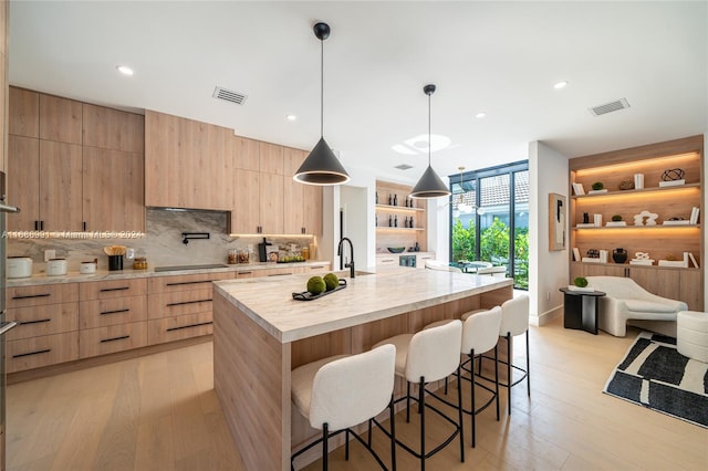 kitchen featuring decorative backsplash, black electric stovetop, hanging light fixtures, a large island, and light hardwood / wood-style floors