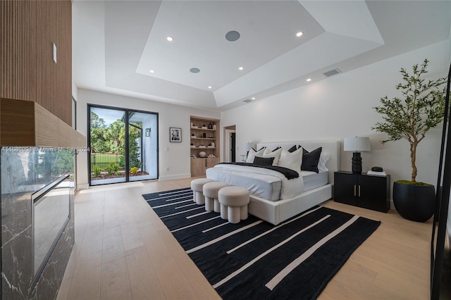 bedroom with light hardwood / wood-style floors, a raised ceiling, and access to outside