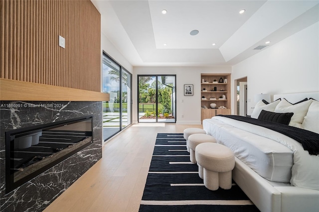 bedroom with a raised ceiling, access to outside, a fireplace, and hardwood / wood-style floors