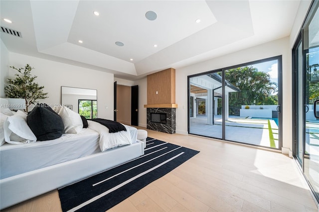 bedroom with light hardwood / wood-style flooring, a tray ceiling, access to outside, and multiple windows