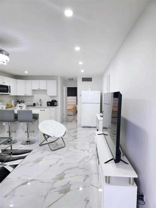 interior space featuring white cabinets, tasteful backsplash, a breakfast bar, sink, and white refrigerator