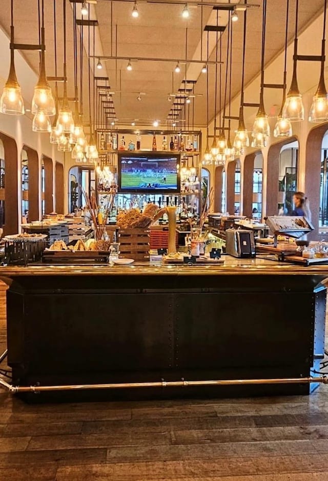 bar with wood-type flooring, a high ceiling, and pendant lighting