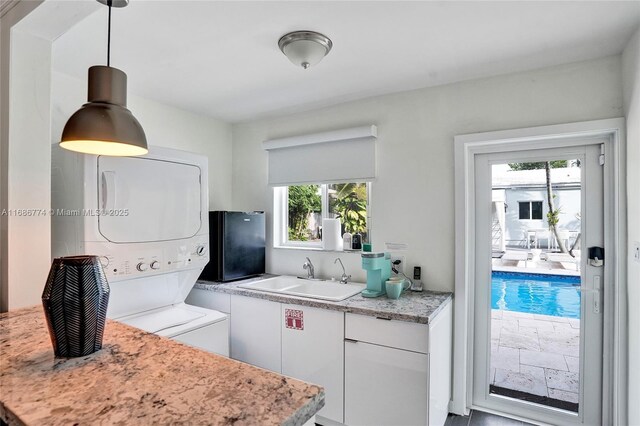 kitchen featuring white cabinetry, stacked washer and dryer, decorative light fixtures, and sink