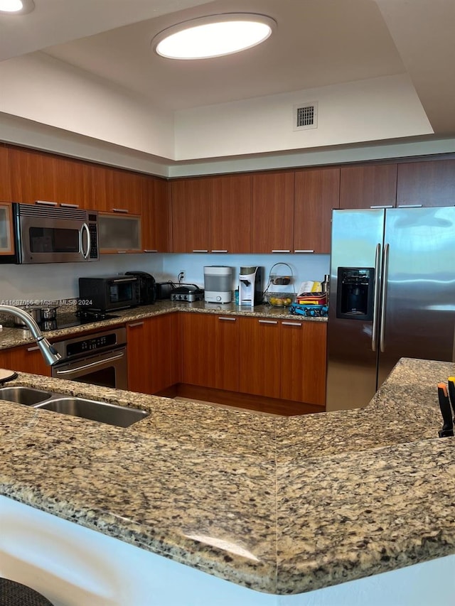 kitchen featuring sink, appliances with stainless steel finishes, kitchen peninsula, and dark stone countertops