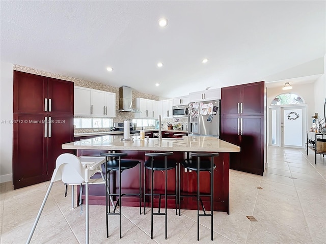 kitchen with a spacious island, wall chimney exhaust hood, a breakfast bar area, stainless steel appliances, and white cabinetry