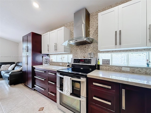 kitchen featuring light tile patterned flooring, range with two ovens, wall chimney exhaust hood, white cabinets, and decorative backsplash