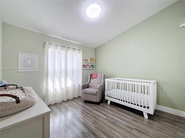 bedroom featuring lofted ceiling, a textured ceiling, a crib, and wood-type flooring