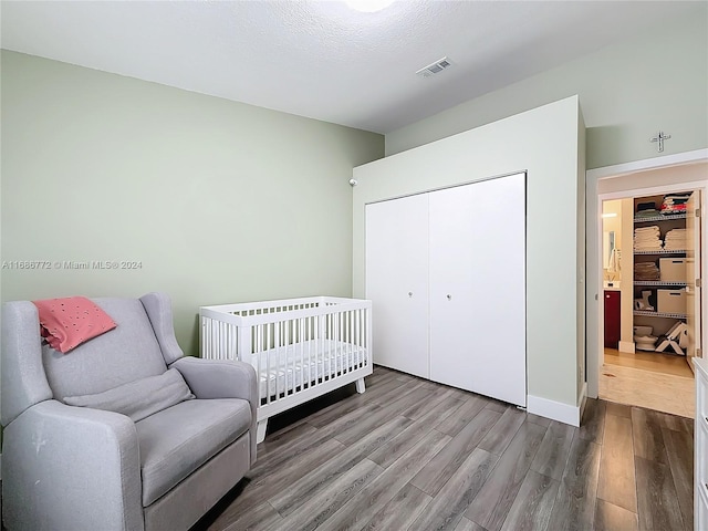 bedroom with a closet, a nursery area, a textured ceiling, and wood-type flooring