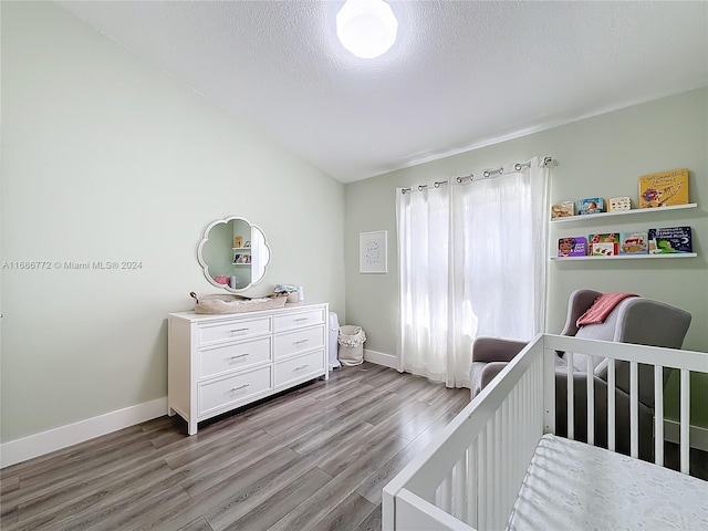 bedroom with light hardwood / wood-style floors, a textured ceiling, and a crib