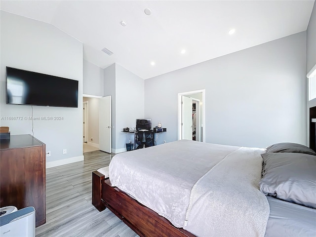 bedroom with light hardwood / wood-style flooring, lofted ceiling, and a walk in closet