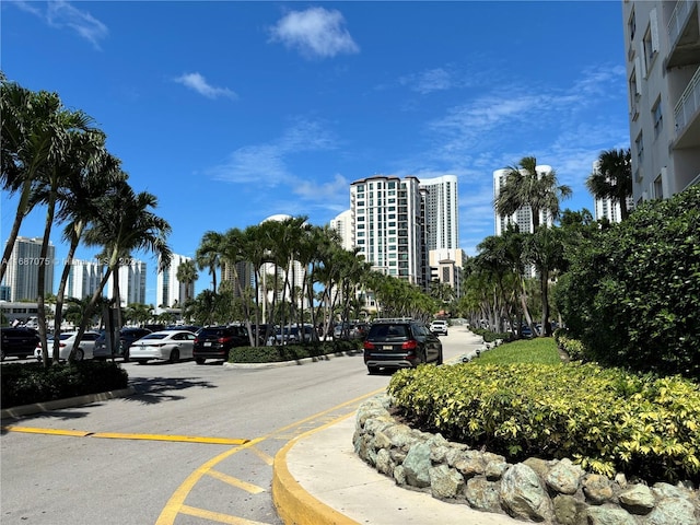 view of asphalt road with curbs, a view of city, and sidewalks