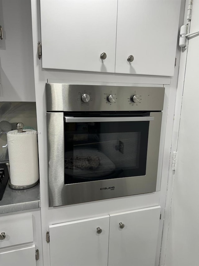 kitchen view of stainless steel oven, white cabinetry, and light countertops