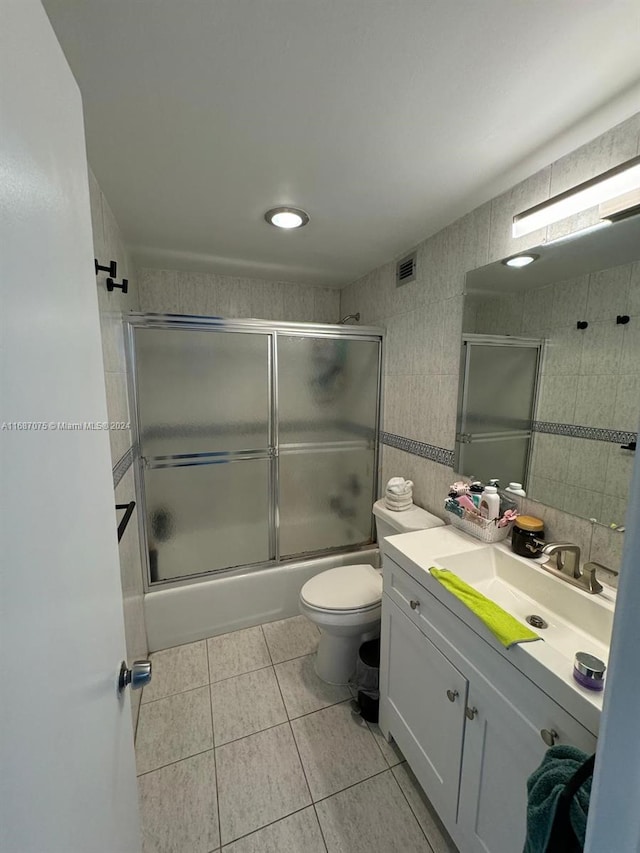 full bathroom featuring bath / shower combo with glass door, tile walls, toilet, vanity, and tile patterned floors