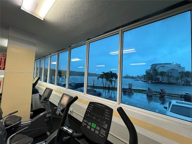 workout area with a textured ceiling and a water view