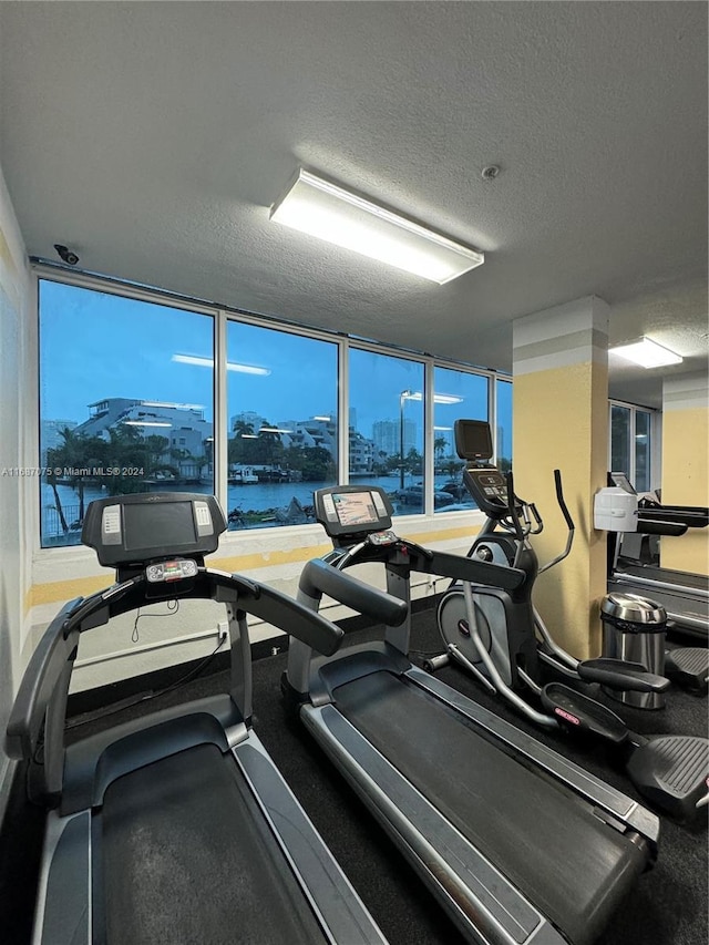 exercise room featuring a water view and a textured ceiling