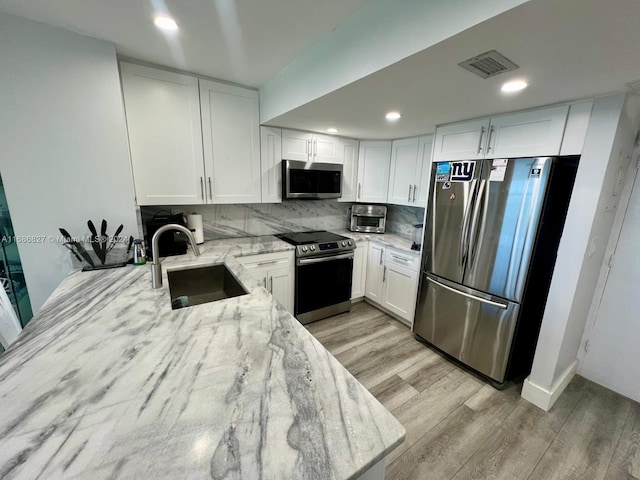 kitchen featuring light stone countertops, appliances with stainless steel finishes, sink, light wood-type flooring, and white cabinetry