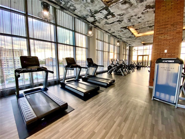 gym with a towering ceiling, expansive windows, and wood-type flooring