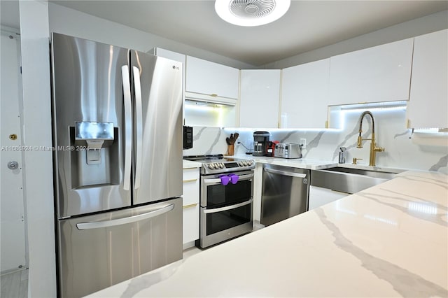 kitchen with white cabinets, tasteful backsplash, light stone counters, sink, and stainless steel appliances