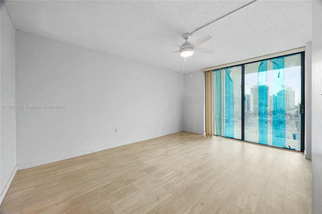 spare room featuring ceiling fan, a textured ceiling, light wood-type flooring, and expansive windows