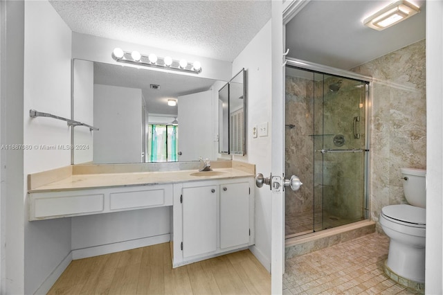 bathroom featuring hardwood / wood-style flooring, toilet, a shower with shower door, vanity, and a textured ceiling