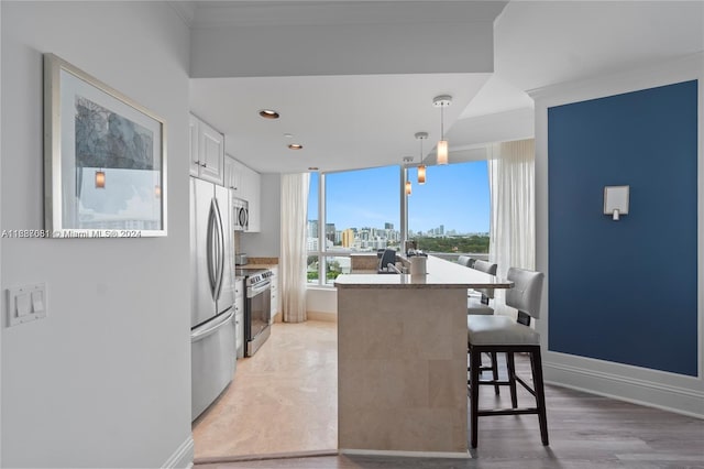 kitchen featuring white cabinetry, pendant lighting, a kitchen bar, appliances with stainless steel finishes, and light wood-type flooring