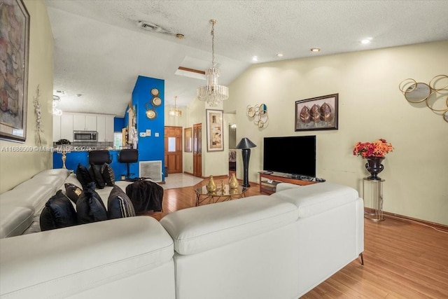 living room featuring light hardwood / wood-style flooring, a textured ceiling, a notable chandelier, and vaulted ceiling