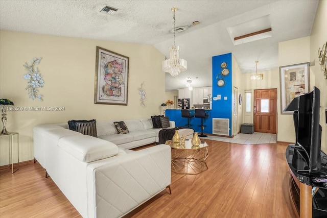 living room featuring lofted ceiling, light hardwood / wood-style flooring, a notable chandelier, and a textured ceiling