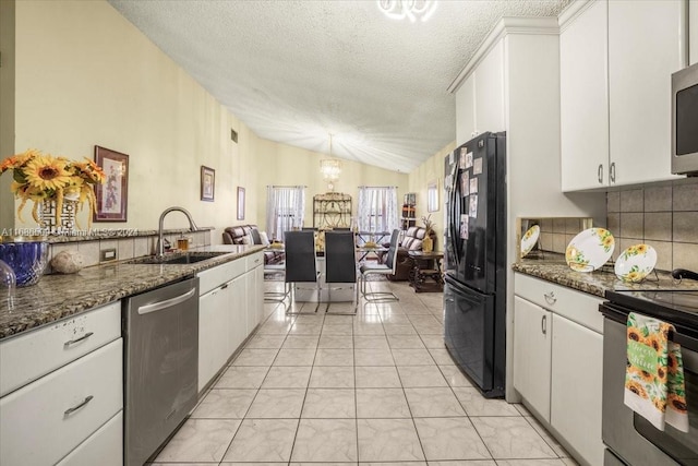 kitchen with lofted ceiling, stainless steel appliances, dark stone countertops, sink, and white cabinets