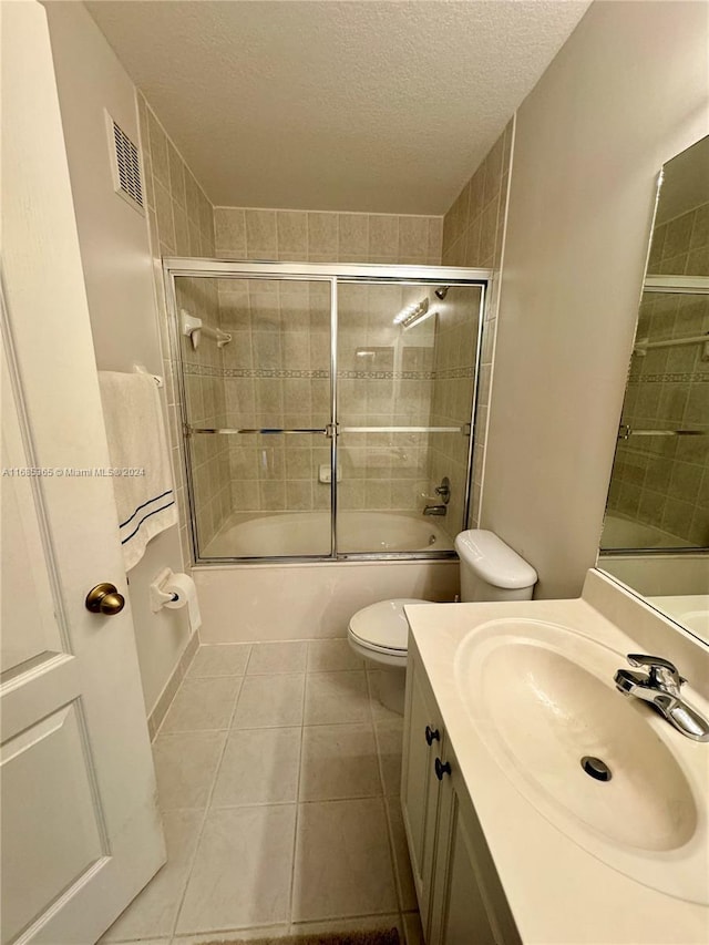 full bathroom with tile patterned floors, bath / shower combo with glass door, a textured ceiling, toilet, and vanity