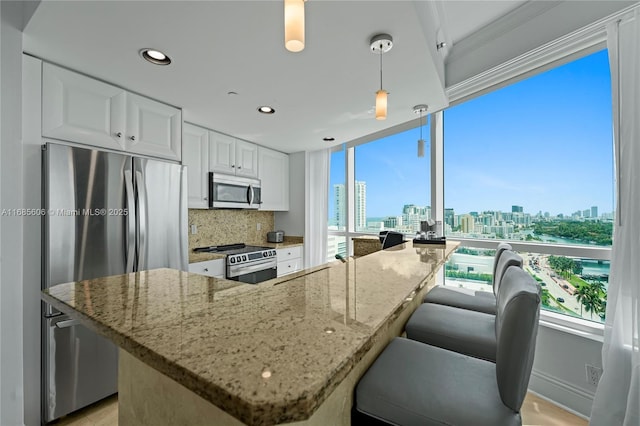 kitchen featuring white cabinetry, backsplash, stainless steel appliances, light stone countertops, and decorative light fixtures