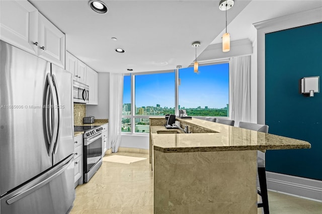 kitchen featuring pendant lighting, a breakfast bar area, stainless steel appliances, light stone countertops, and white cabinets