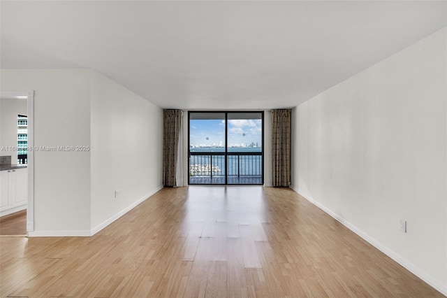 empty room featuring a wall of windows and light hardwood / wood-style flooring