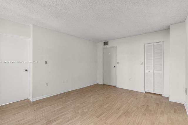 spare room with a textured ceiling and light hardwood / wood-style floors