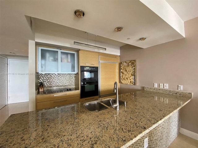 kitchen with kitchen peninsula, tasteful backsplash, stone counters, double oven, and sink