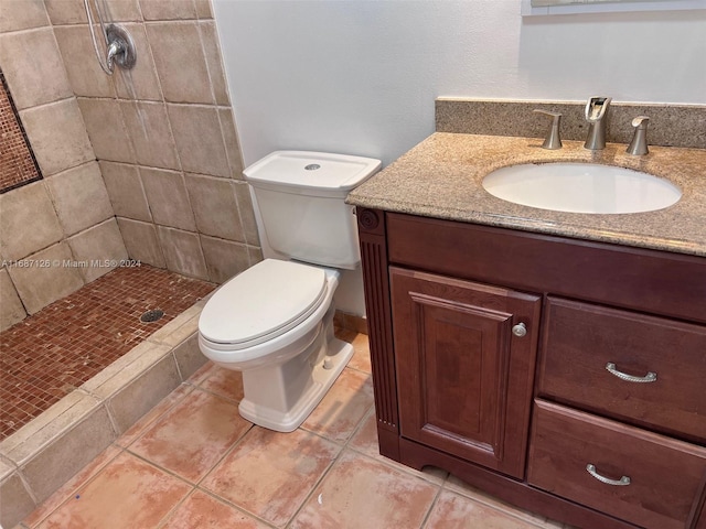 bathroom with tiled shower, tile patterned flooring, vanity, and toilet