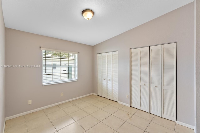 unfurnished bedroom featuring vaulted ceiling, light tile patterned floors, and two closets