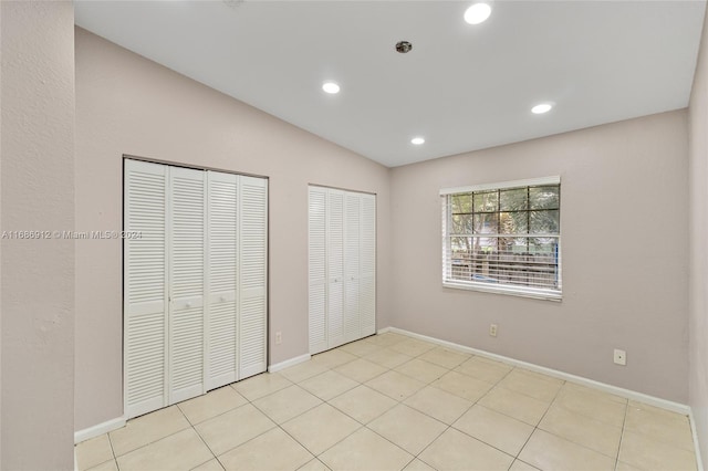 unfurnished bedroom with vaulted ceiling, light tile patterned floors, and multiple closets