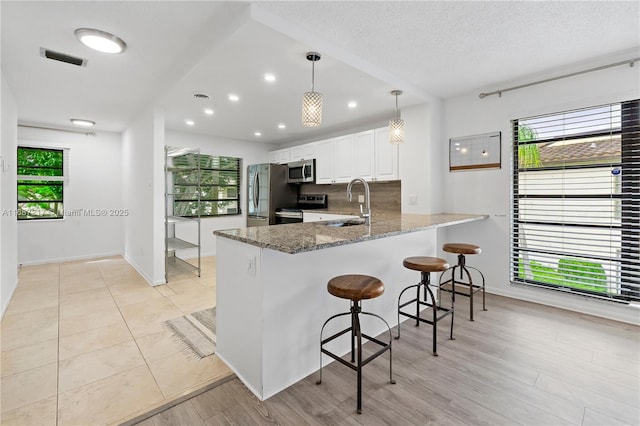 kitchen with kitchen peninsula, appliances with stainless steel finishes, dark stone counters, white cabinets, and hanging light fixtures