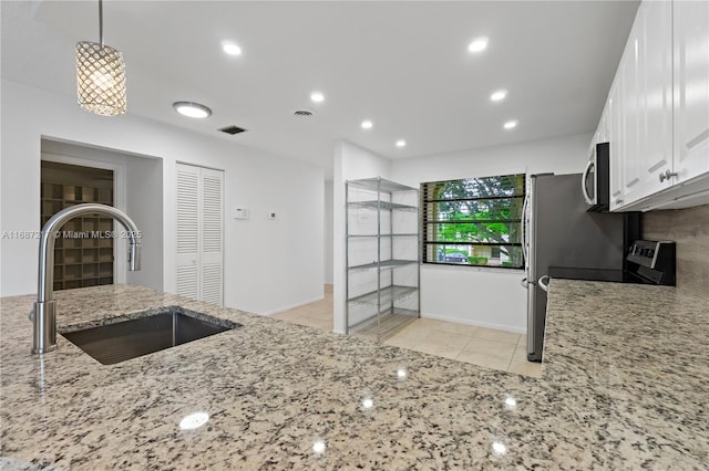 kitchen featuring sink, light tile patterned floors, decorative light fixtures, light stone counters, and white cabinetry